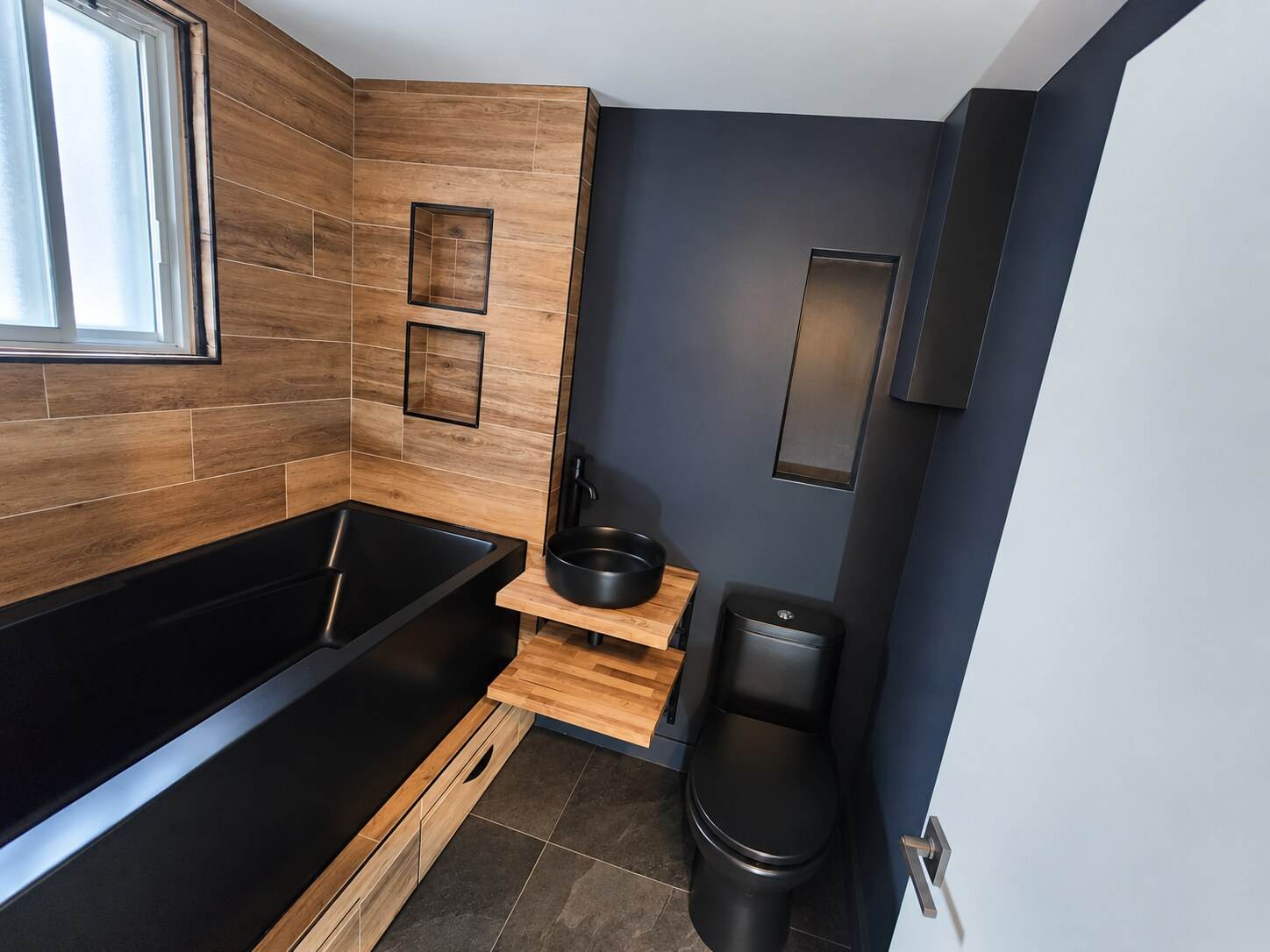 Renovated bathroom with a black bathtub, wood-look tile and matching cabinetry